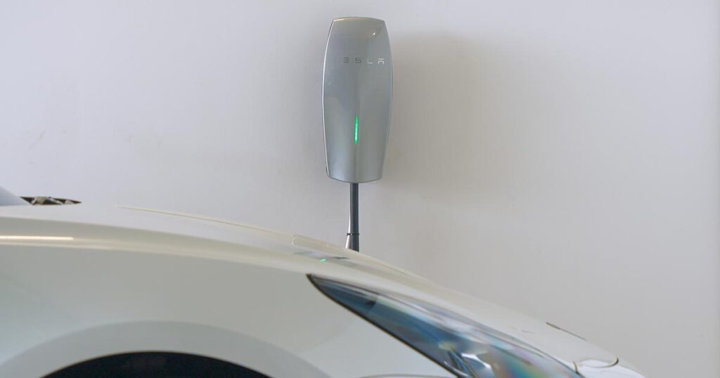 Tesla Wall Connector installed on a garage wall with a white electric vehicle parked below