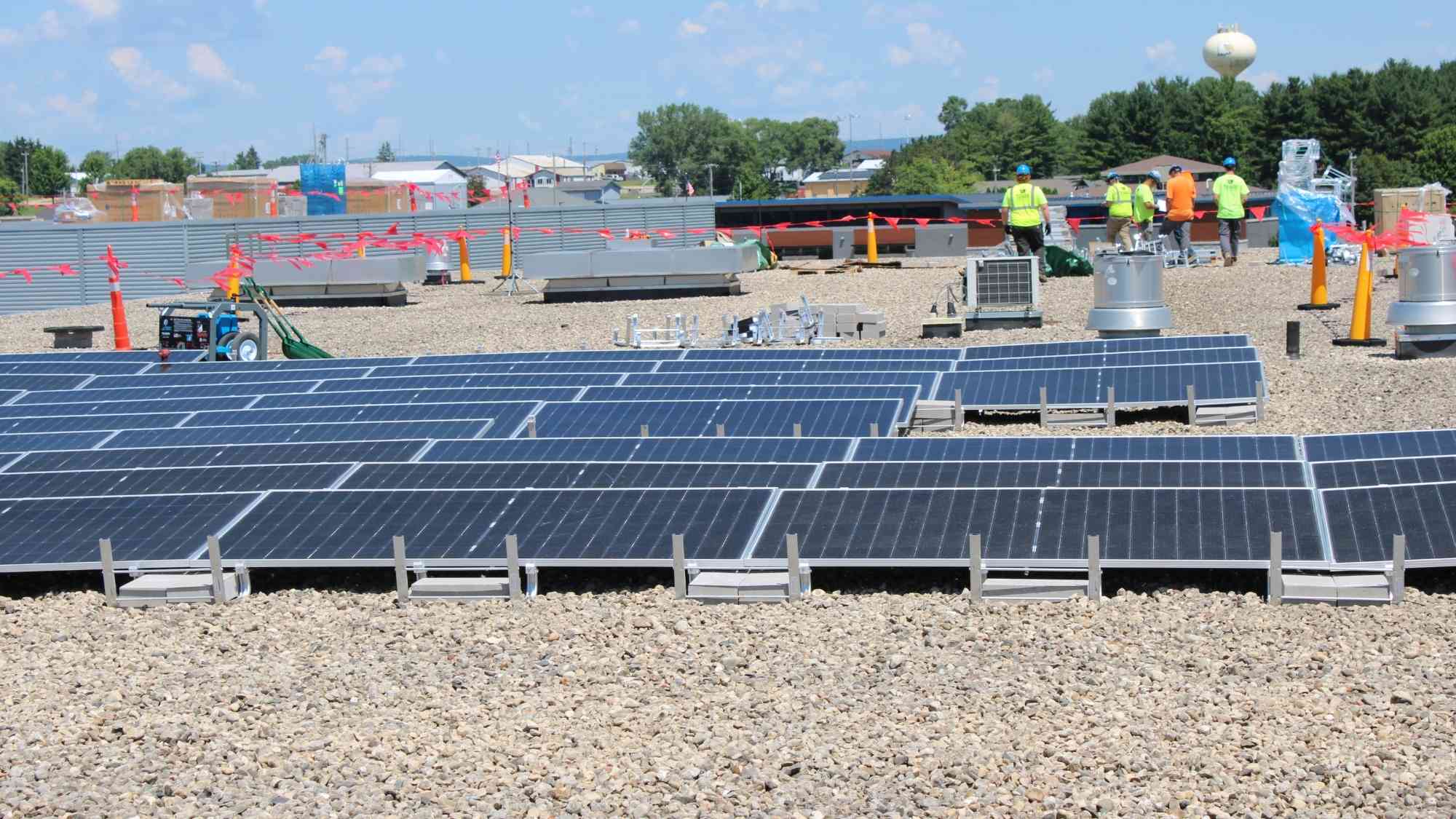 Rows of ballasted solar panels installed across the rooftop of Bridges Elementary School with crews working in the background.
