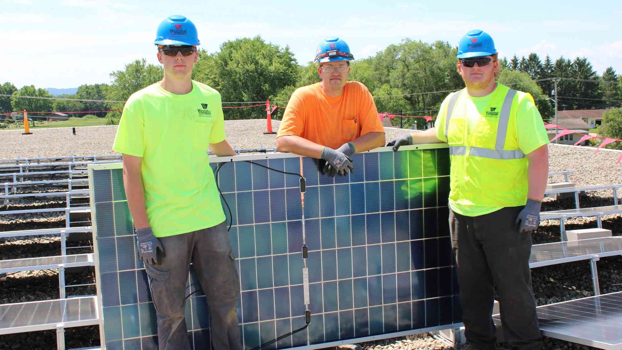 Three Westphal & Company electricians standing with a solar panel during rooftop solar installation at Bridges Elementary School in Sauk City, Wisconsin.