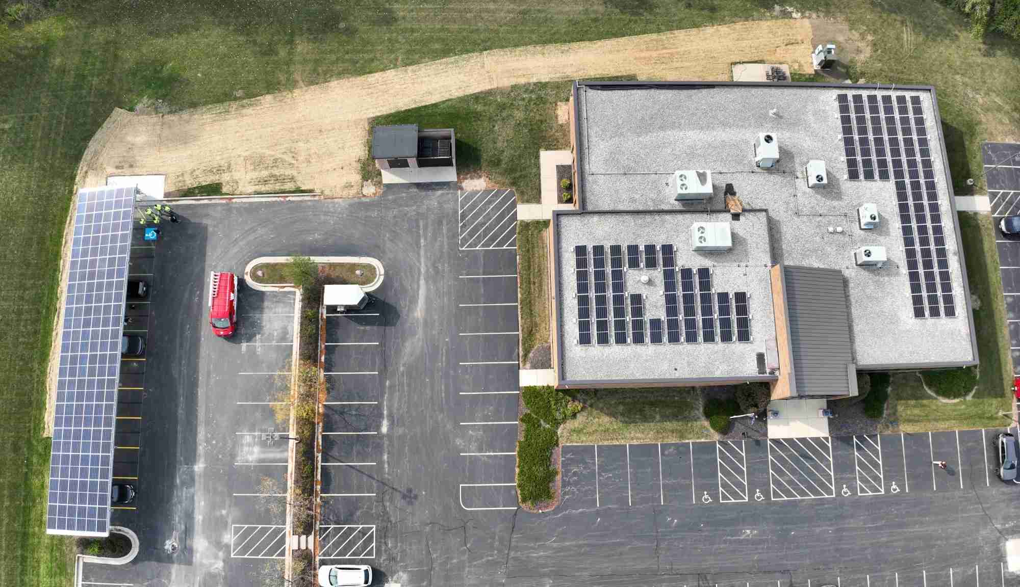 Aerial view of the IBEW Local 494 building with rooftop solar panels and adjacent solar canopy installation area.