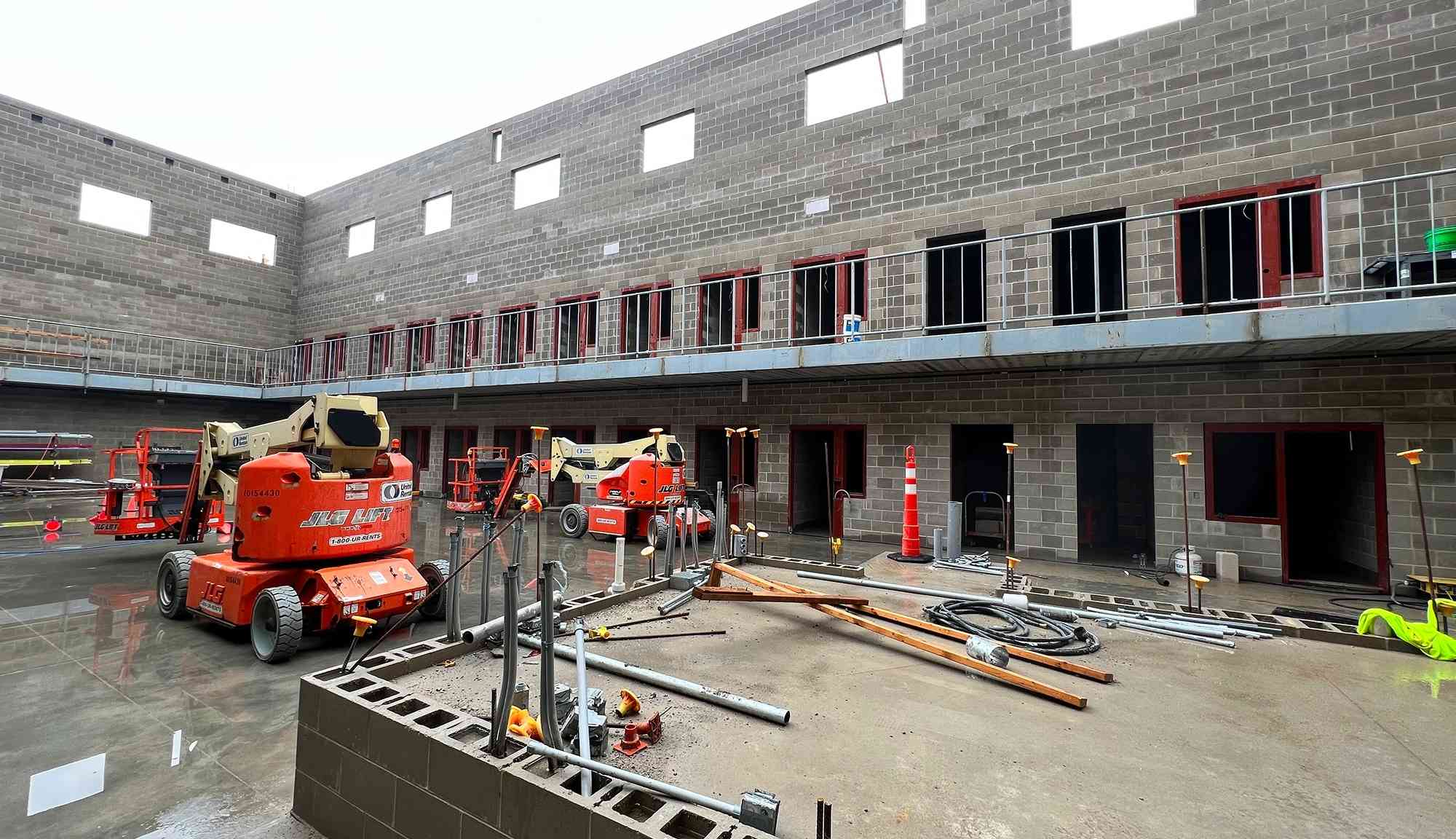 Active construction site showing masonry walls, aerial lifts, and building infrastructure under construction.