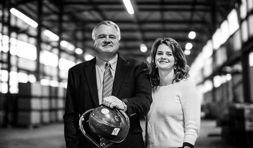 Two business leaders standing in an industrial facility, one holding a hard hat, representing leadership in electrical construction.