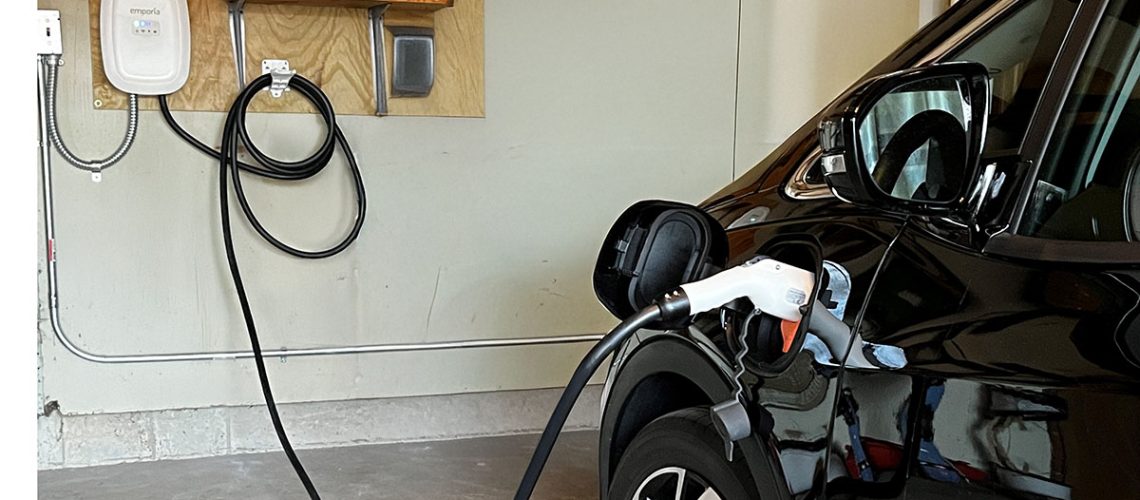 Black electric vehicle charging in a residential garage with a wall-mounted Emporia home EV charger.